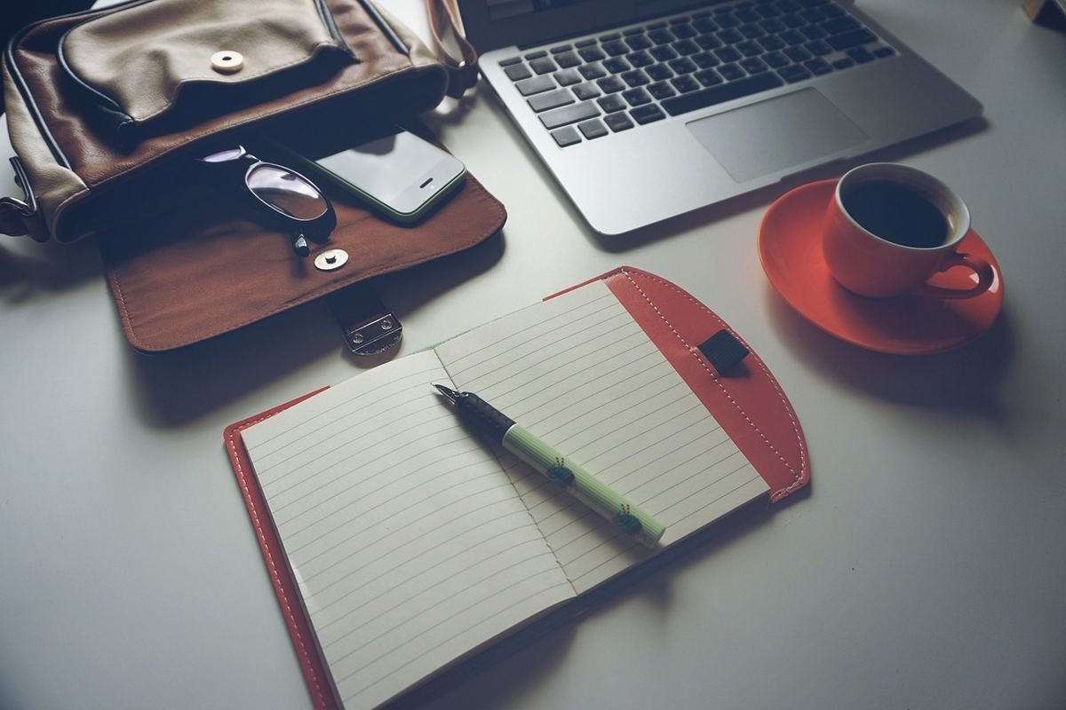 Un ordinateur portable, une tasse de café sur une soucoupe, un agenda ouvert avec un stylo, et un portefeuille sur une table