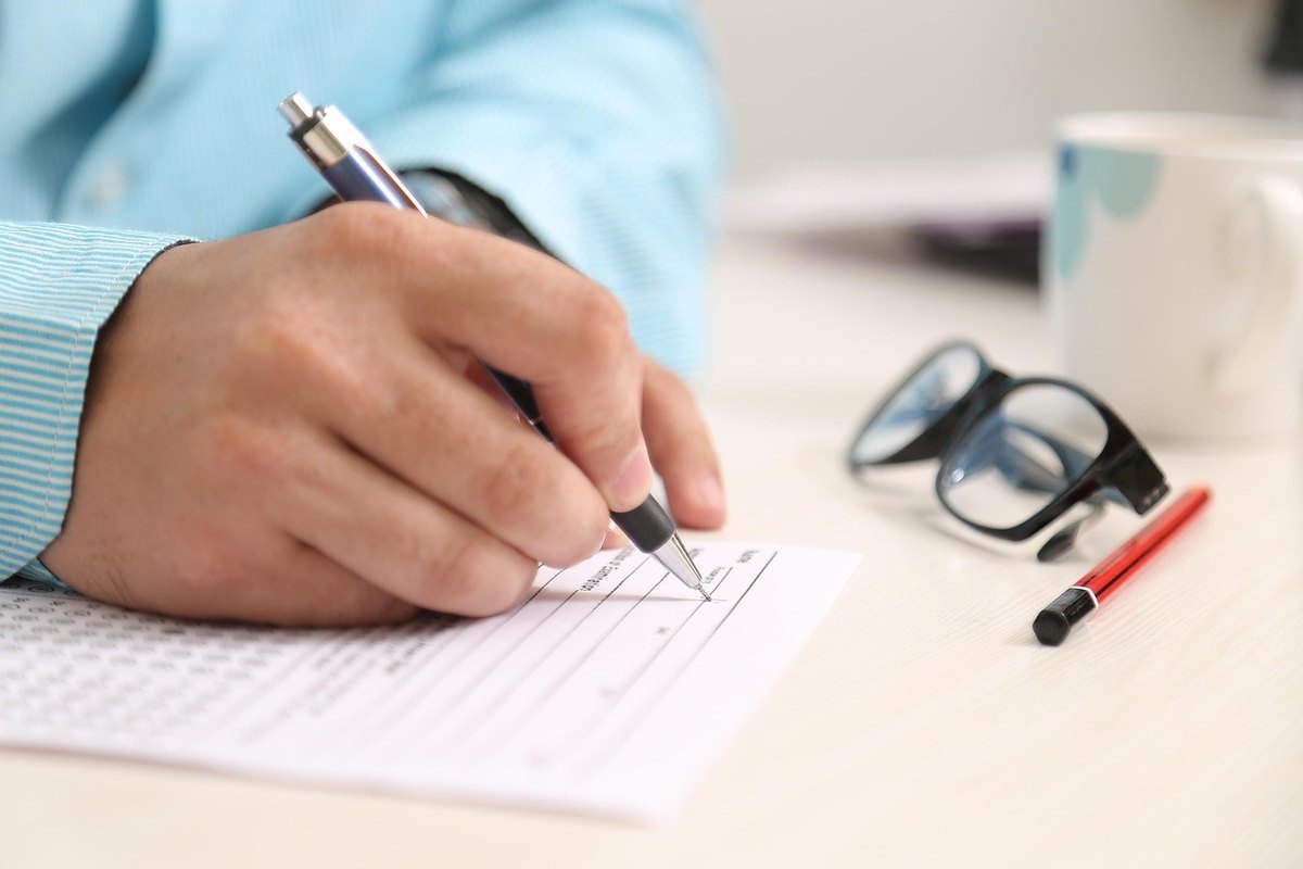 Mains écrivant sur feuille avec lunettes et stylo à côté