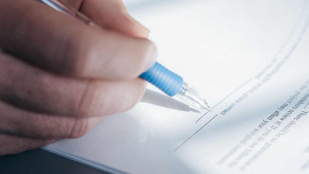 Main tenant un stylo bleu, en train de signer un document