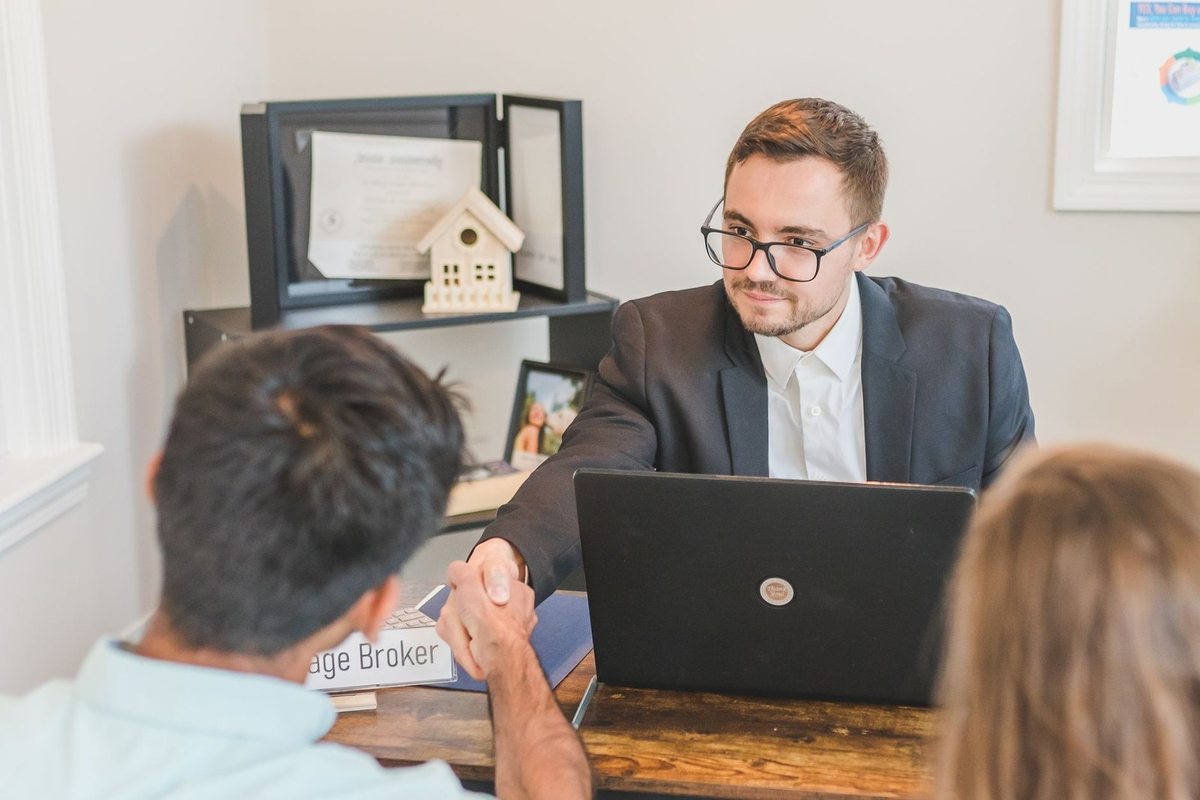 Homme en costume saluant un autre individu devant un ordinateur portable dans un bureau
