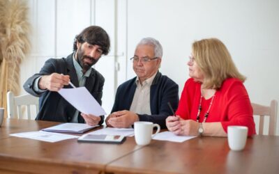 Trois individus analysent des papiers lors d'une réunion dans une pièce avec une table en bois