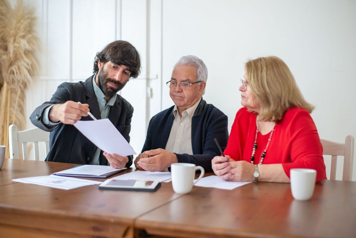 Trois individus analysent des papiers lors d'une réunion dans une pièce avec une table en bois