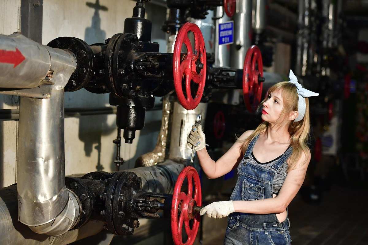 Femme en denim ajuste une vanne rouge sur tuyauterie industrielle
