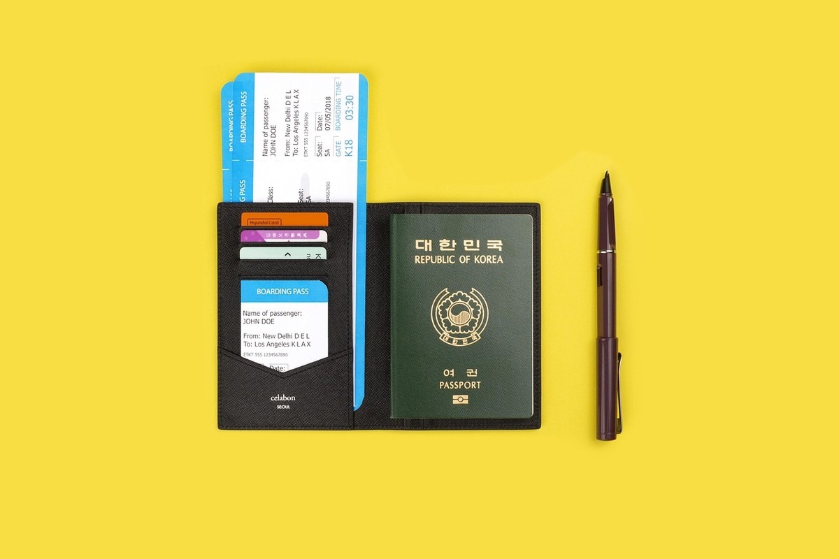 Passeport noir ouvert, documents et carte à l'intérieur, stylo à côté sur fond jaune