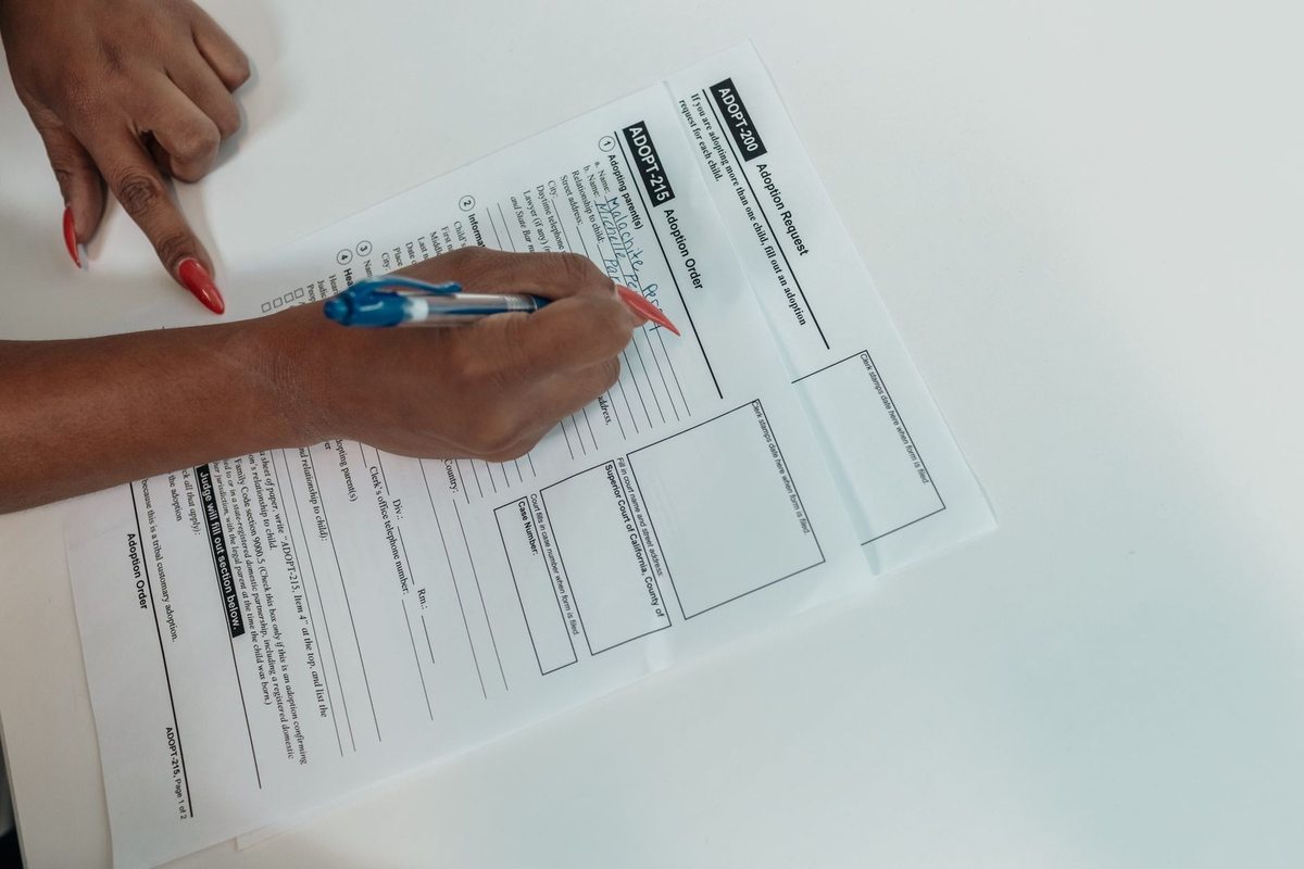 Main gauche pointant vers document, main droite écrivant dessus avec stylo bleu
