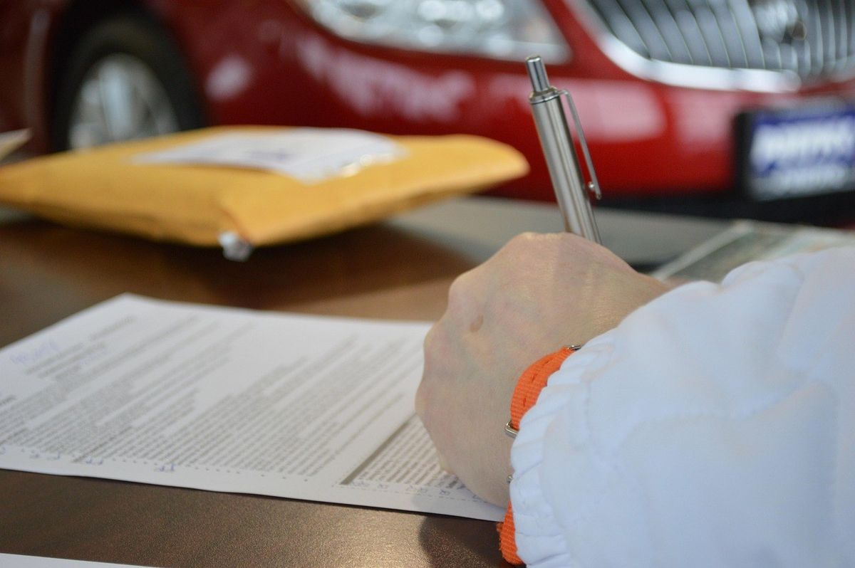 Main tenant un stylo sur un document, enveloppe jaune et voiture rouge en arrière-plan