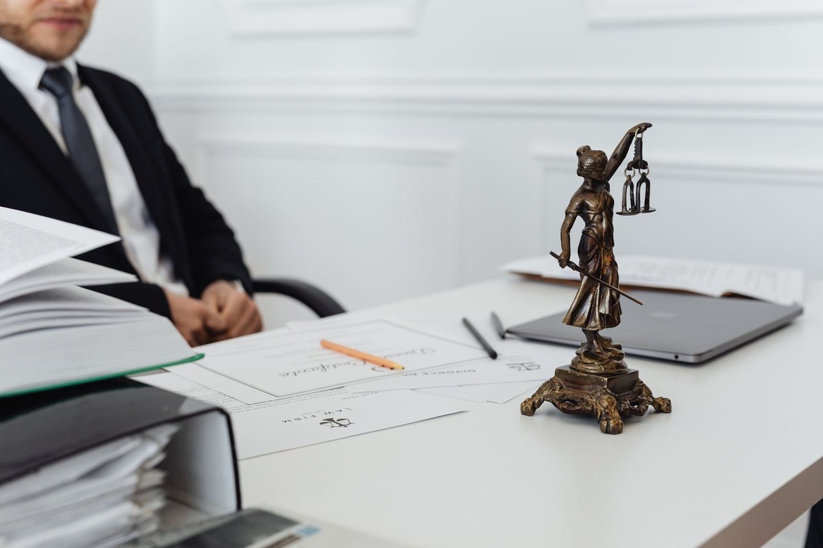 Homme en costume assis à un bureau avec une statue de la justice, des papiers et un ordinateur portable