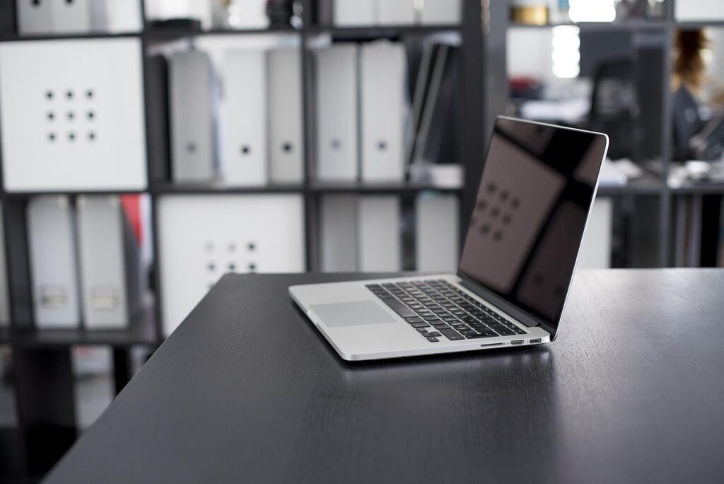 Un ordinateur portable ouvert sur un bureau, classeurs derrière