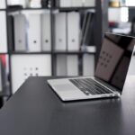 Un ordinateur portable ouvert sur un bureau, classeurs derrière