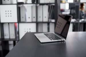 Un ordinateur portable ouvert sur un bureau, classeurs derrière